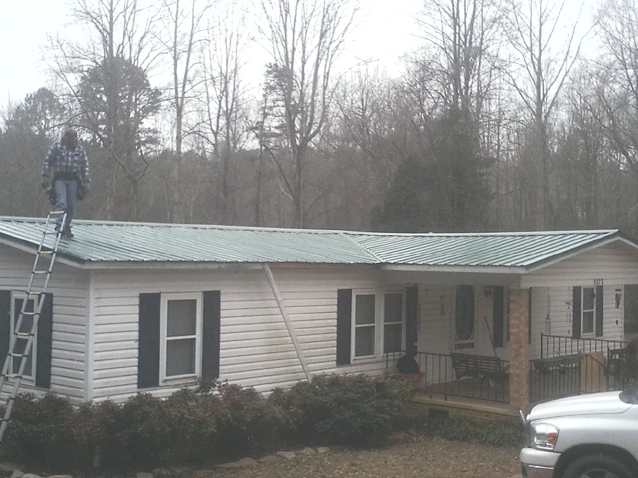 Worker on a ladder beside a new green metal roof on a ranch home in Winfield