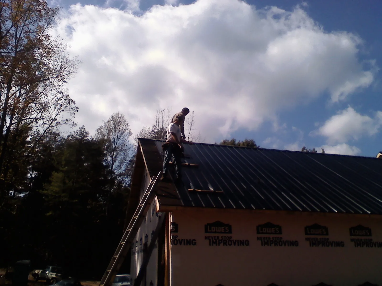Roofer fastening dark metal panels high against a cloudy sky, from a Roof Inspection job in Winfield